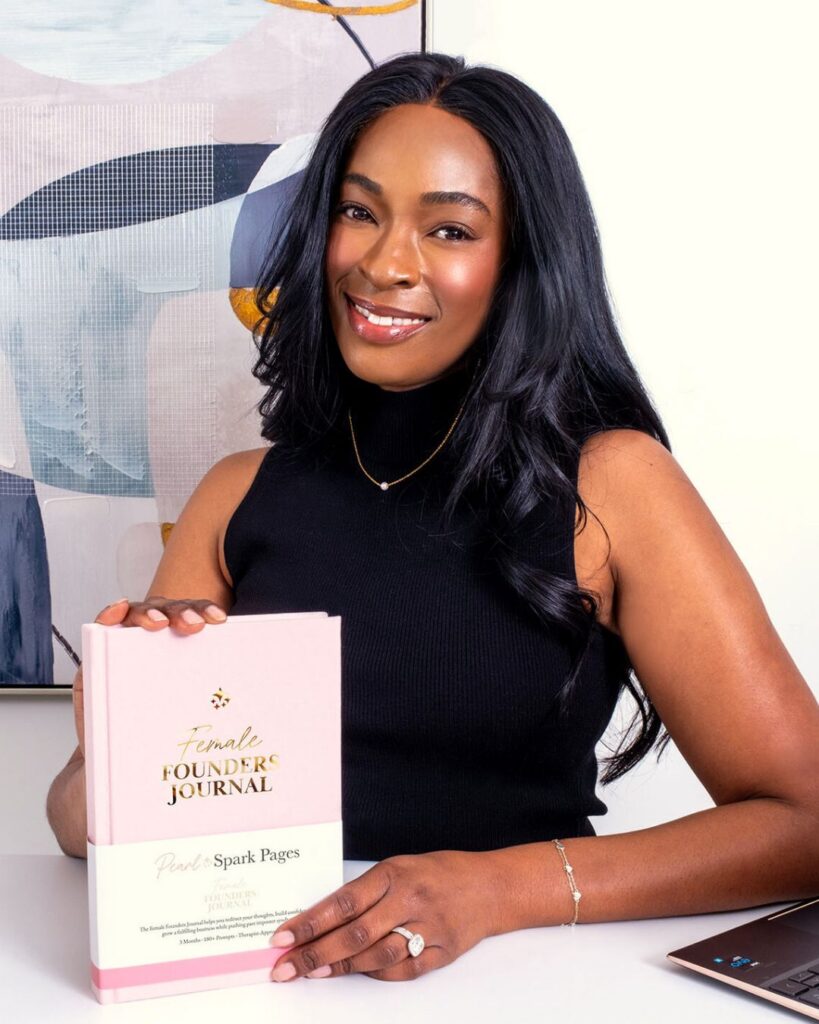 Lisa Simone Simons holding the Female Founders Journal, smiling at camera in a black tank top.
