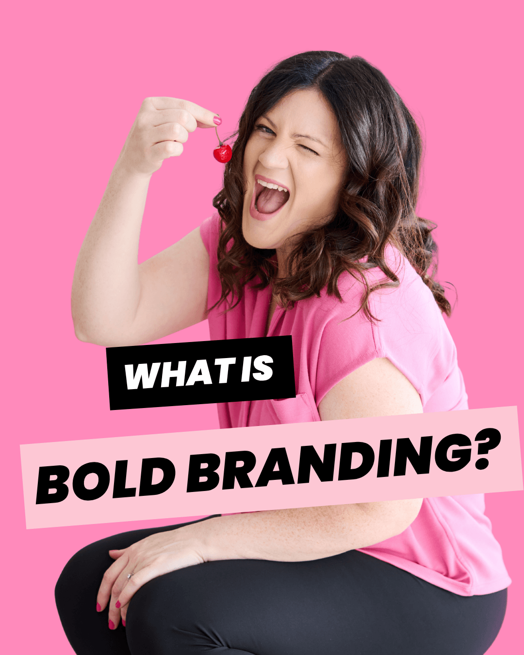 Emily, Canadian bold branding strategist and designer, holding a pink cherry and winking in a pink button up shirt